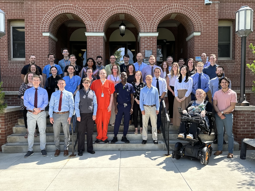 All members of the program stand on the steps of a brick building